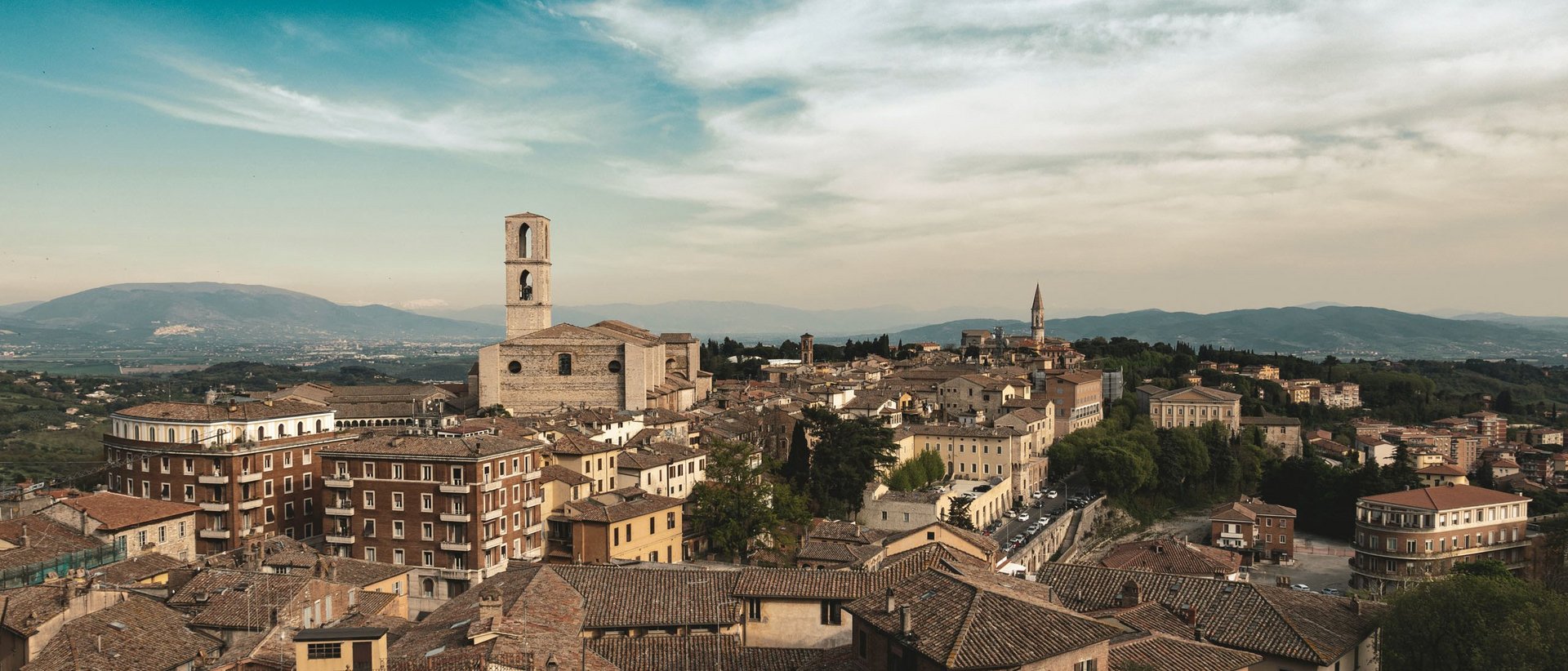 Sehenswürdigkeiten in Assisi und Umgebung Panorama der Stadt mit historischen Gebäuden und Kirchtürmen bei teilweise bewölktem Himmel