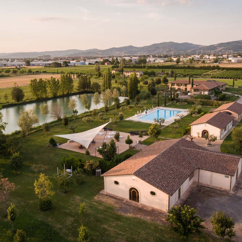 Un resort vicino ad Assisi indimenticabile Veduta aerea di azienda agricola con piscina e lago circondata da campi verdi e montagne