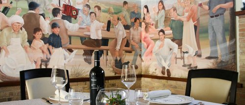 La missione di Valle di Assisi Tavolo apparecchiato con vino davanti a murales di persone in festa