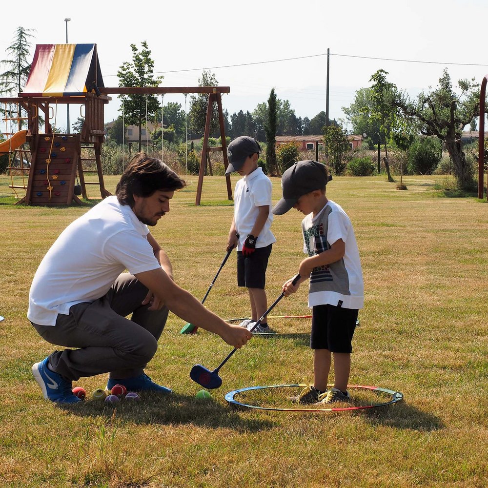 Valle di Assisi, un luogo per momenti in famiglia Uomo insegna a due bambini a giocare a golf nel parco giochi all'aperto