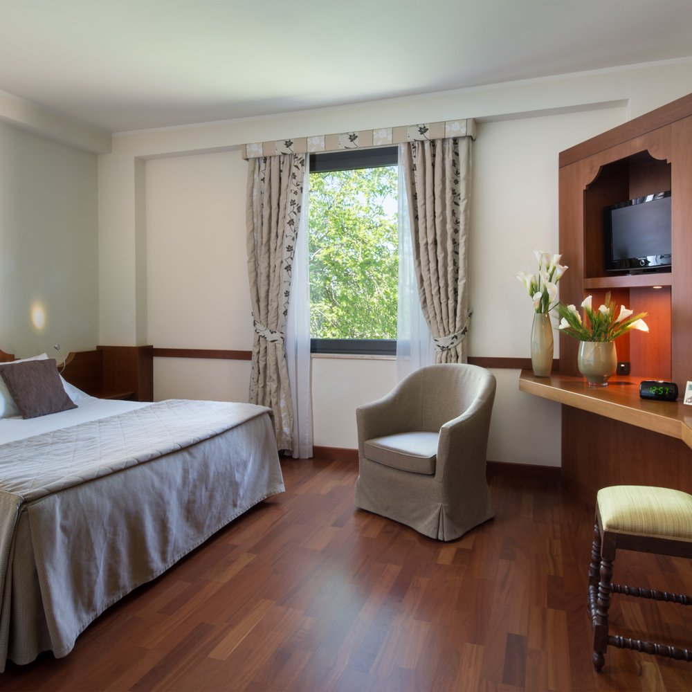Un hotel accessibile, in Umbria, con una marcia in più Camera d'hotel con letto matrimoniale, poltrona, scrivania in legno e finestra con tende