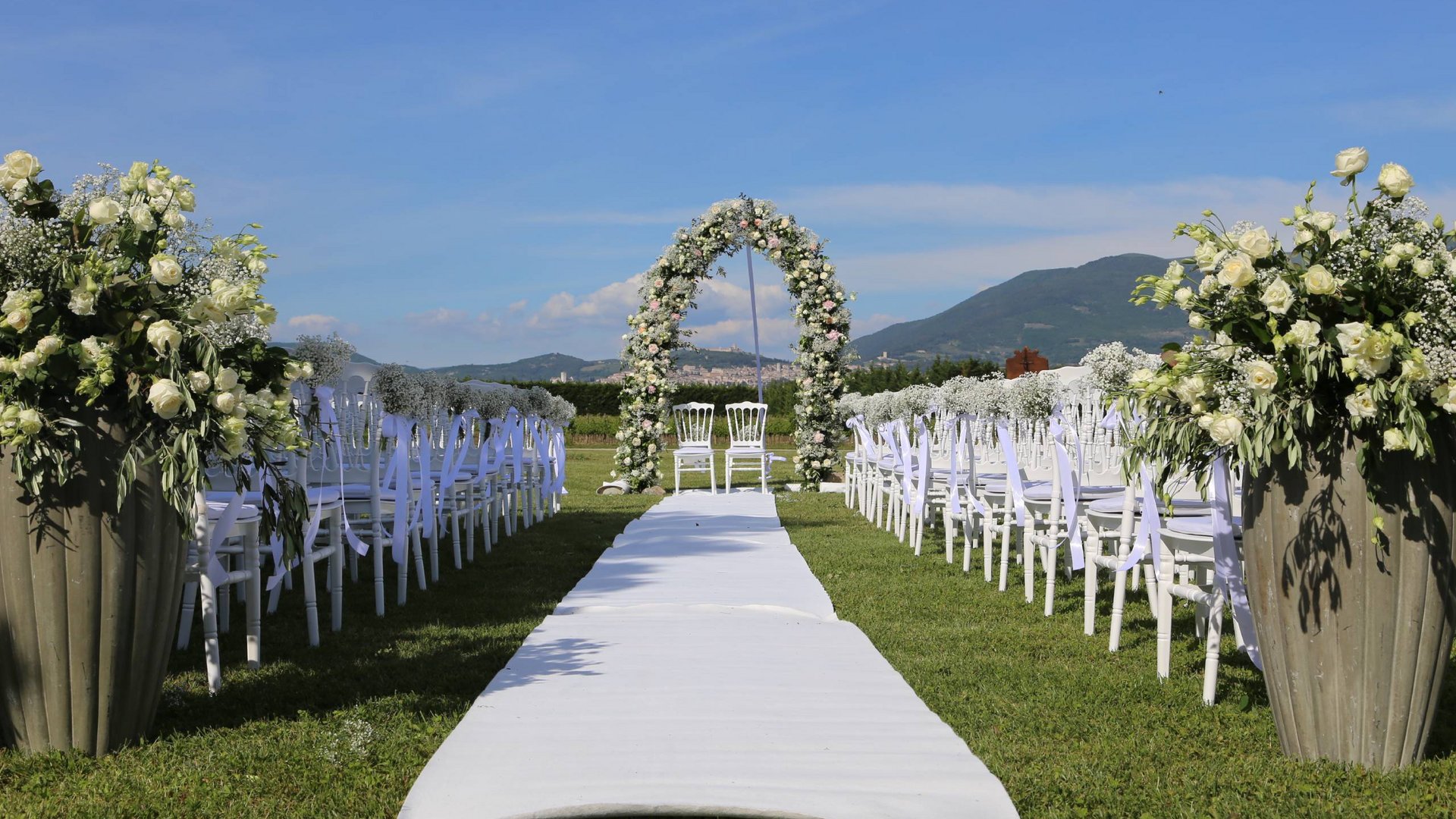 La vostra location per matrimoni ad Assisi Allestimento esterno per cerimonia di matrimonio con sedie bianche e arco floreale