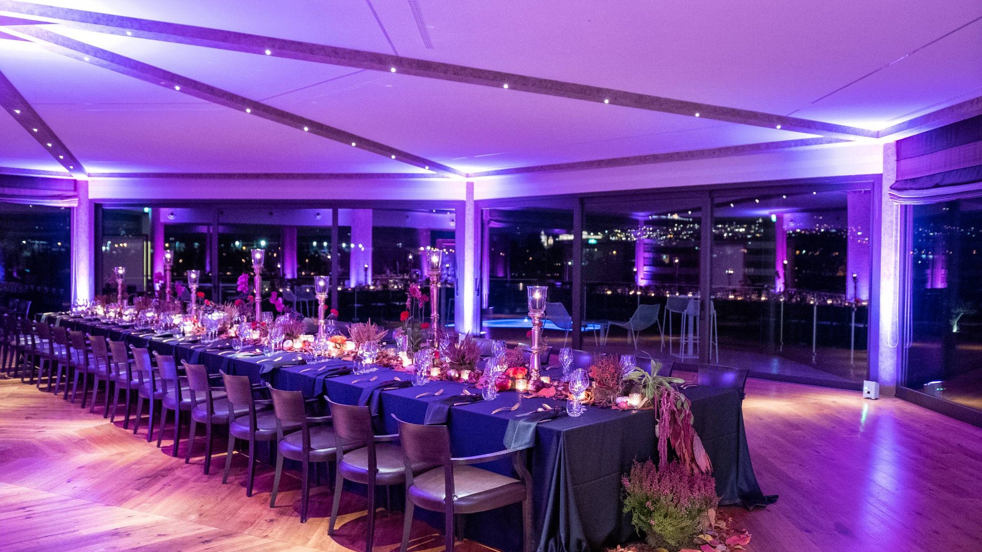 La vostra location per matrimoni ad Assisi Tavolo lungo allestito per cena elegante con luci viola e decorazioni floreali