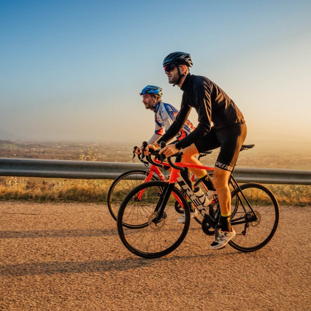 Vacanze Bike ad Assisi unico Italy bike hotels in Umbria Due ciclisti su strada in collina al tramonto con abbigliamento da ciclismo