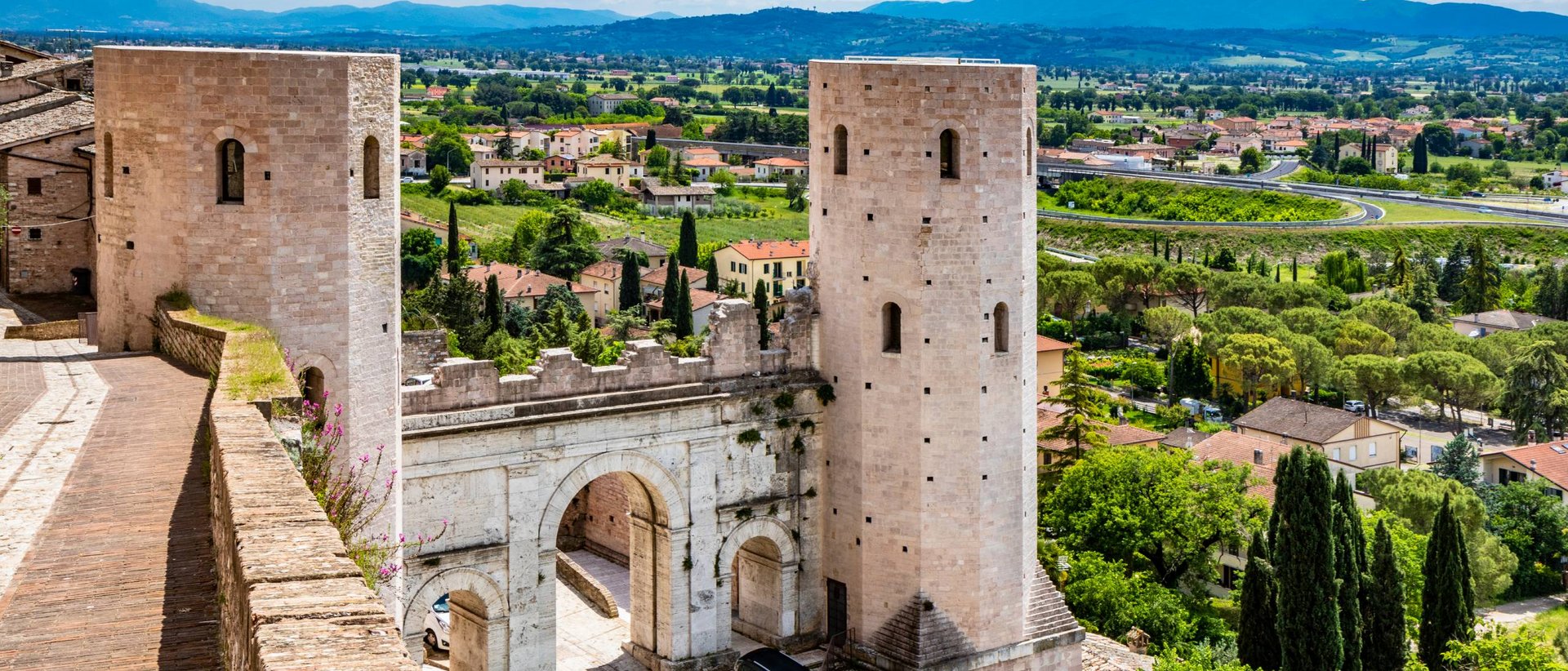 La Basilica di San Francesco ad Assisi Vista della porta medievale con due torri in pietra e paesaggio verde intorno