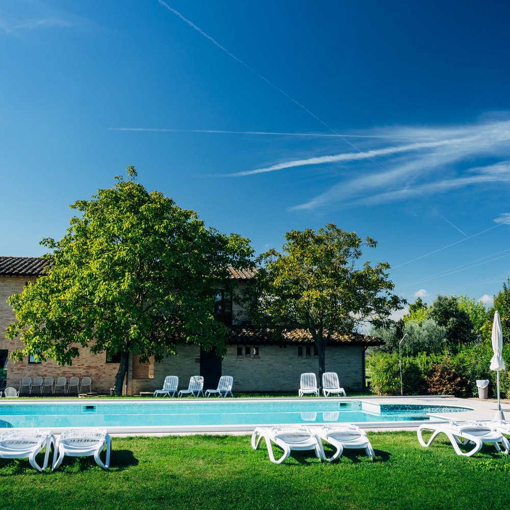 Villa ad Assisi con piscina privata, vacanze nel cuore dell'Umbria Piscina all'aperto con lettini e ombrelloni in un giardino soleggiato davanti a una casa