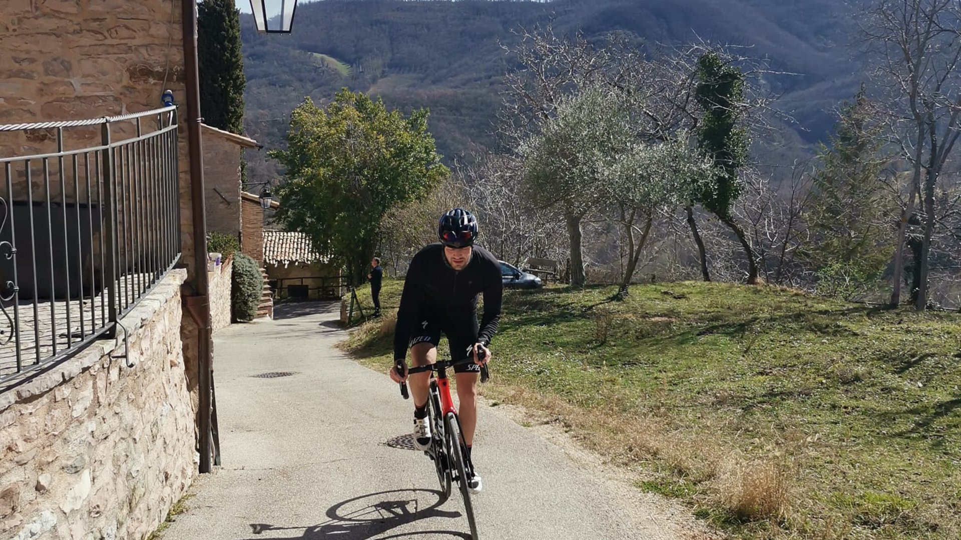 Vacanze Bike ad Assisi unico Italy bike hotels in Umbria Ciclista in abbigliamento nero in salita accanto a casa in pietra e colline