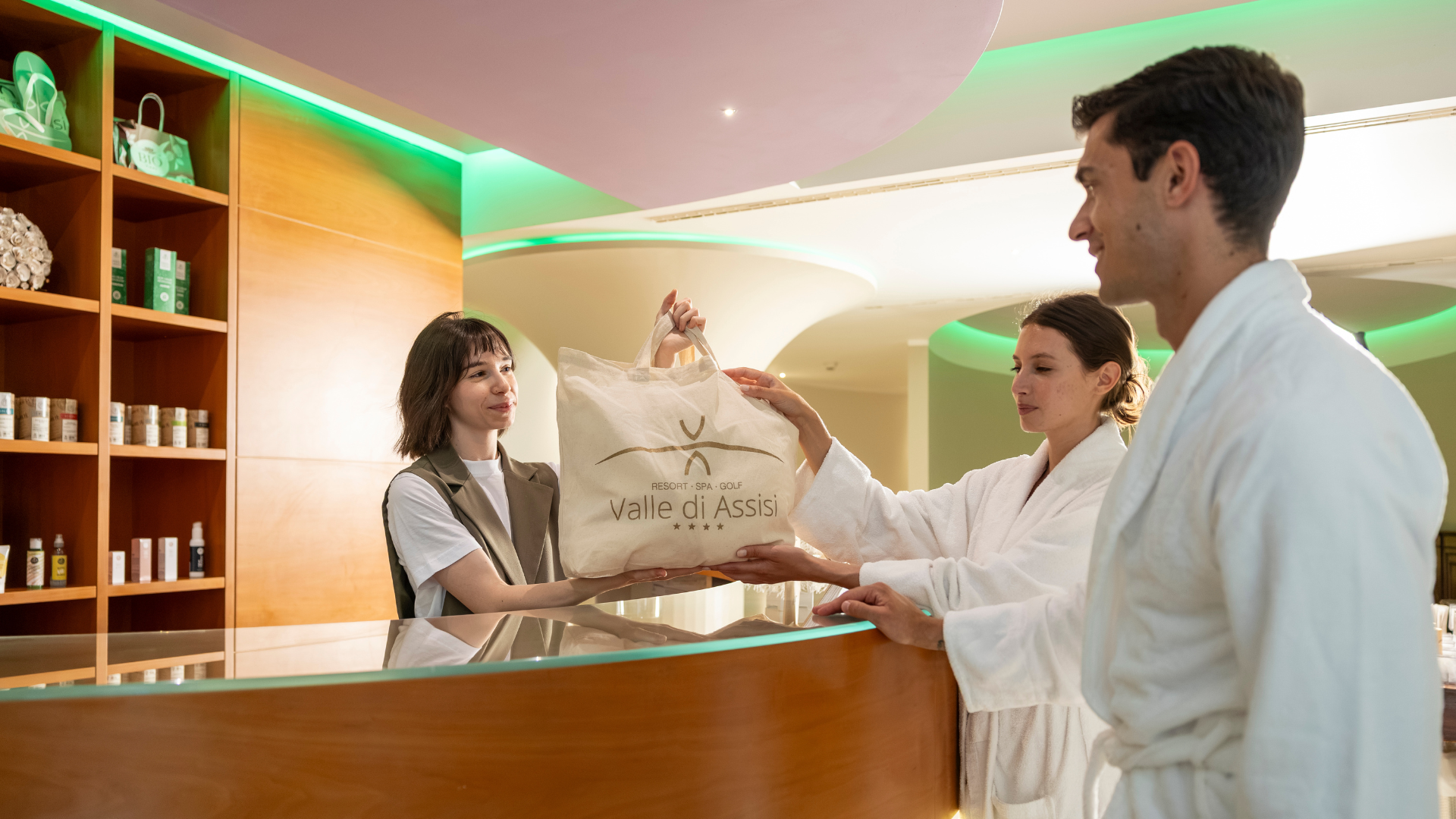 Una spa per bambini in Umbria? Eccola qui Assisi Cantico SPA a Santa Maria degli Angeli, la provincia di Perugia più bella! Receptionist consegna una borsa Valle di Assisi a due ospiti in accappatoio
