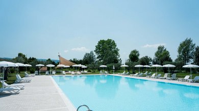 Vacanza vicino ad Assisi, Resort Hotel com Campo da Padel Tennis Bike Hotel 3 piscine campo da calcetto. Piscina vuota all'aperto con lettini e ombrelloni bianchi in un parco verde