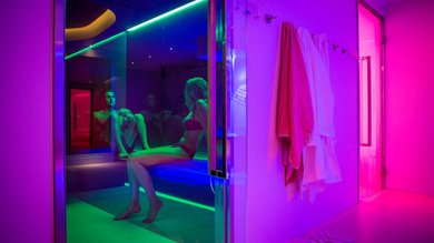 Epifania 2025 in Social SPA Due persone sedute in una sauna con illuminazione colorata e accappatoi appesi