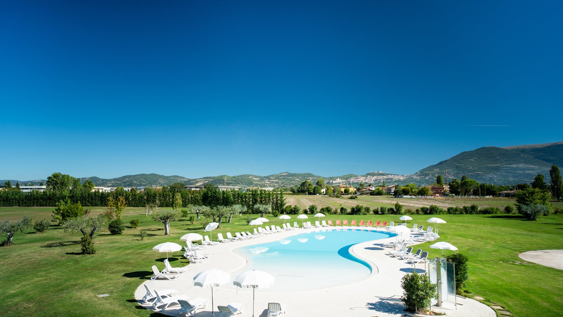 Vacanze Bike ad Assisi unico Italy bike hotels in Umbria Piscina a forma di fagiolo con sedie a sdraio bianche e ombrelloni in un prato verde