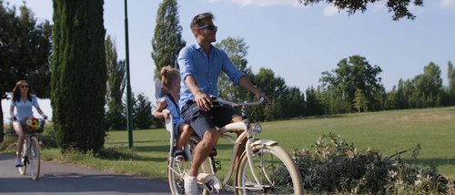 La missione di Valle di Assisi Uomo in bicicletta con bambina seduta dietro durante una passeggiata in un parco soleggiato