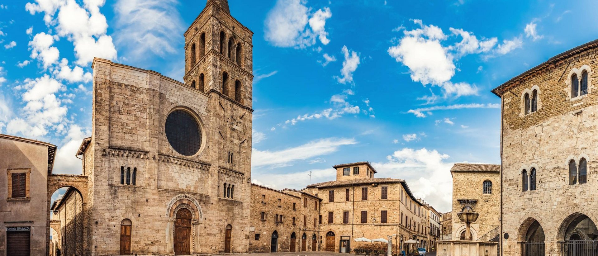 Sehenswürdigkeiten in Assisi und Umgebung Historischer Platz mit Kirche und Brunnen unter klarem Himmel