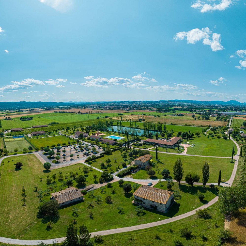 Valle di Assisi: un resort per matrimoni ad Assisi Vista aerea di una campagna con edifici, campi verdi e piscina