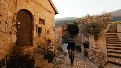 Vacanze Bike ad Assisi unico Italy bike hotels in Umbria Ciclista che pedala in un vicolo storico di pietra al tramonto