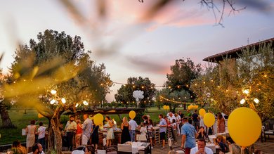 Cena Sotto le Stelle Festa all'aperto di sera con palloncini gialli e persone che socializzano