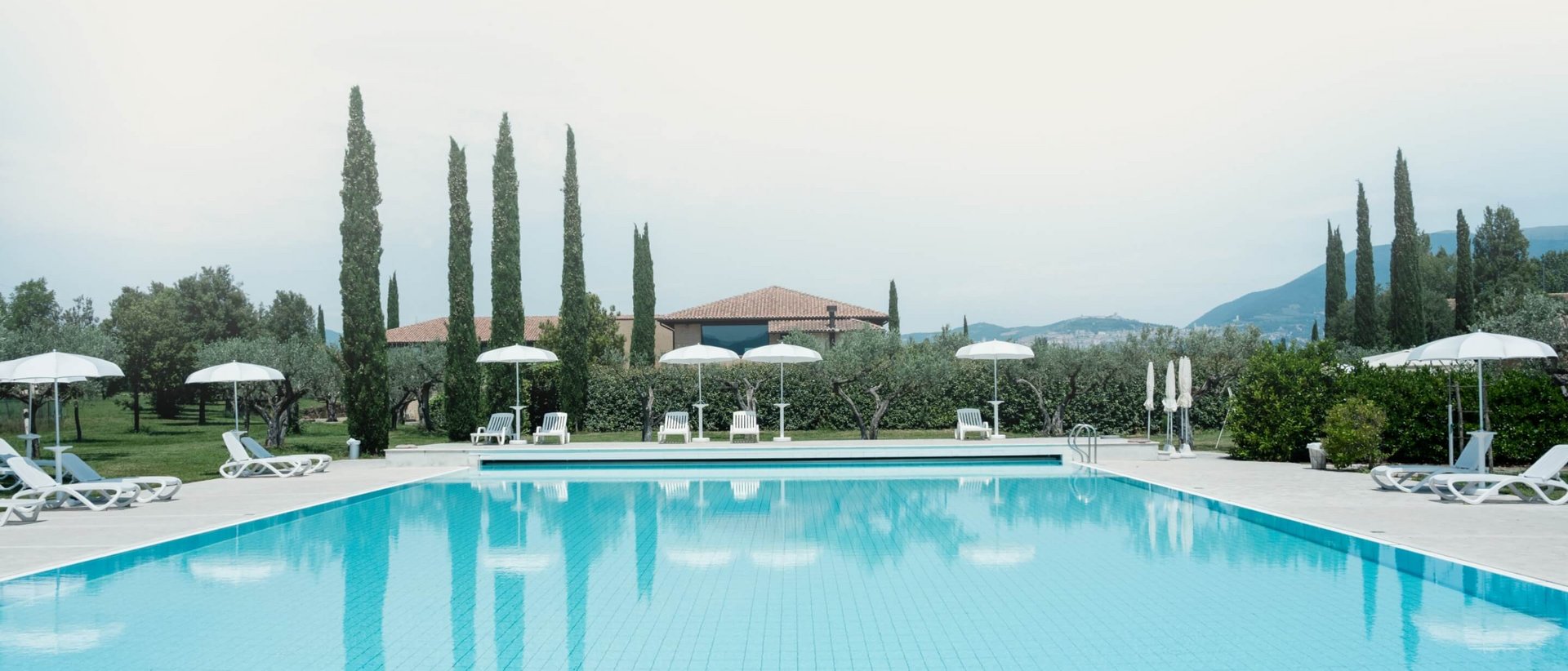 La missione di Valle di Assisi Piscina all'aperto con sdraio e ombrelloni in un giardino verde.