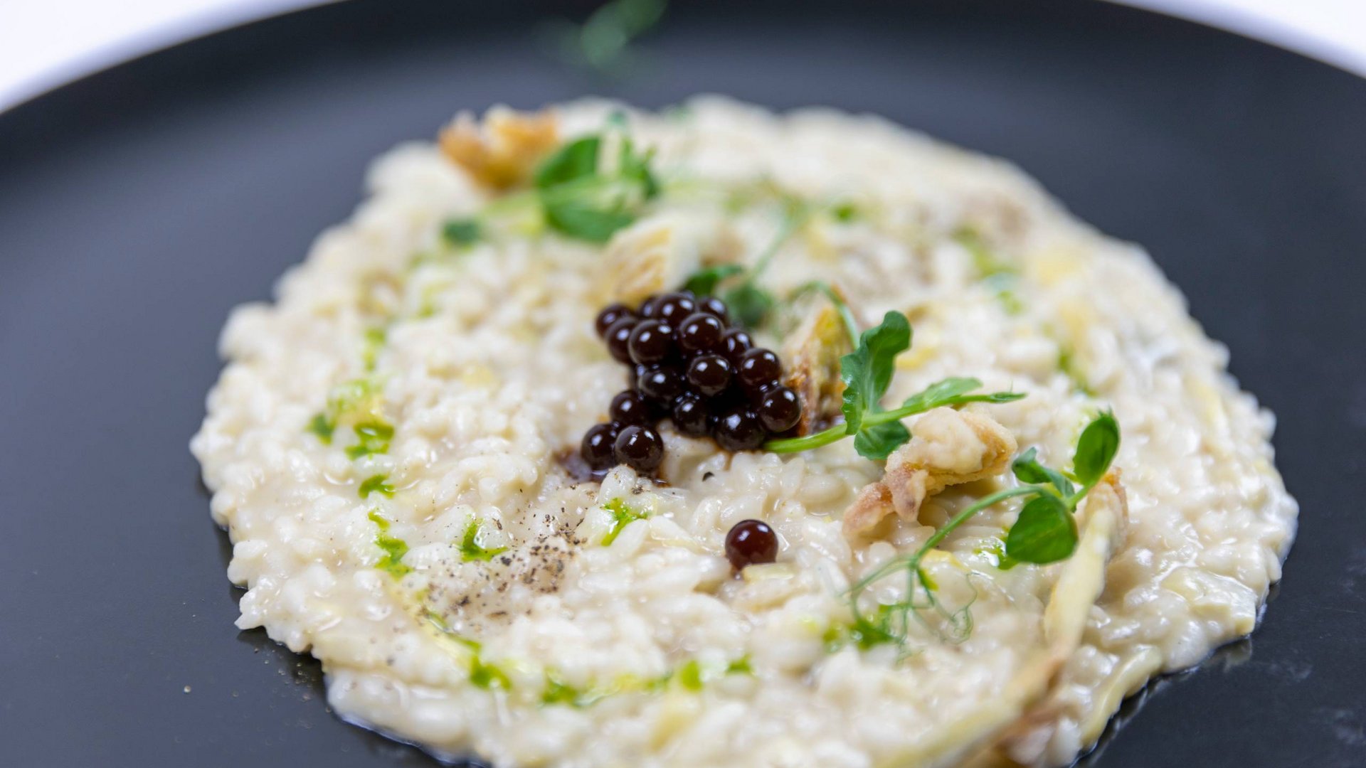 Hotel con ristorante vicino ad Assisi: benvenuti al Recanto Risotto cremoso guarnito con palline di gel nero e erbe fresche su piatto nero