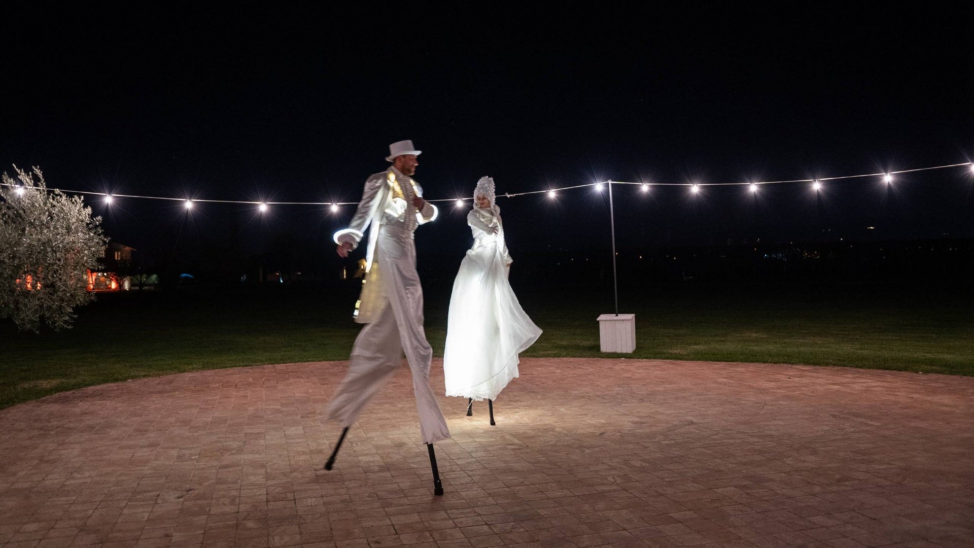 La vostra location per matrimoni ad Assisi Due artisti su trampoli con costumi bianchi illuminati di notte all'aperto
