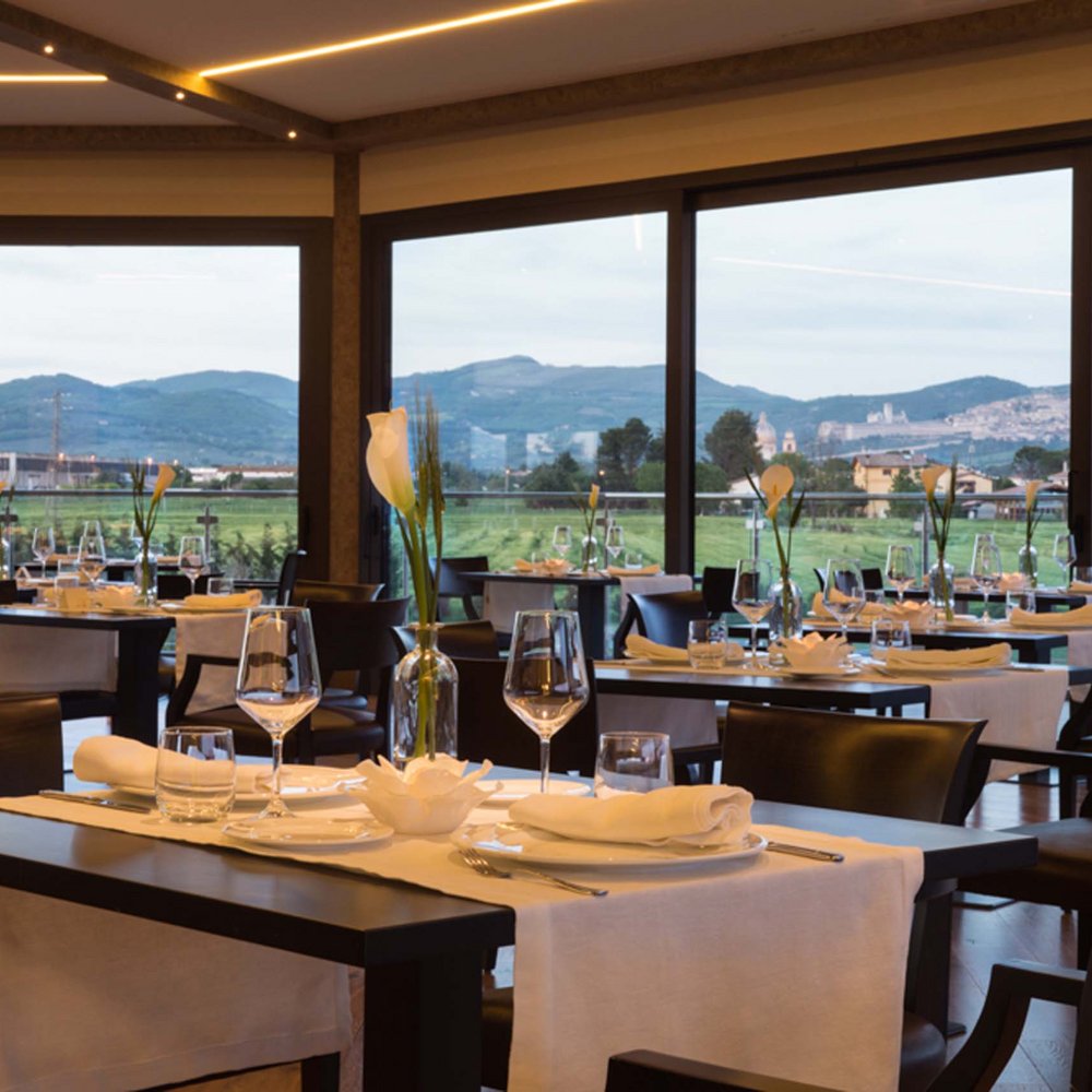 Hotel con ristorante vicino ad Assisi: benvenuti al Recanto Ristorante elegante con tavoli apparecchiati e vista sulle colline