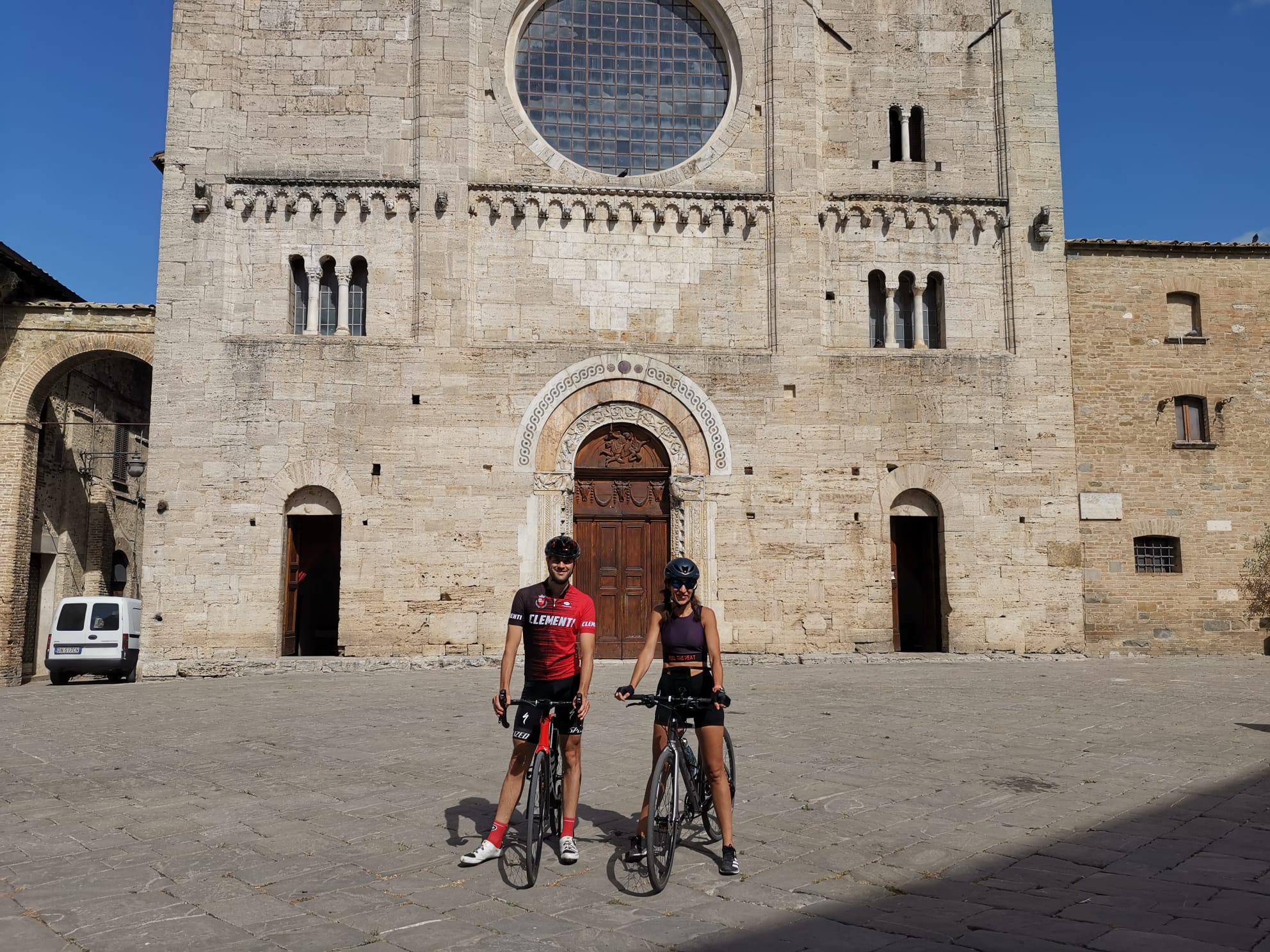 Vacanze Bike ad Assisi unico Italy bike hotels in Umbria Due ciclisti con bici davanti a una chiesa storica di pietra sotto il sole